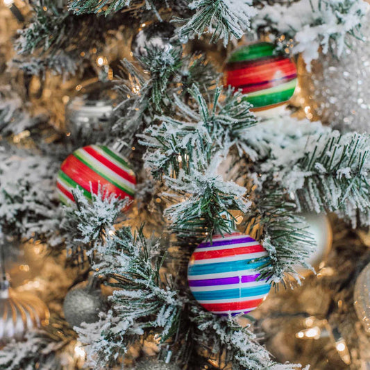 Colorful striped ornaments on a snow flocked Christmas tree.
