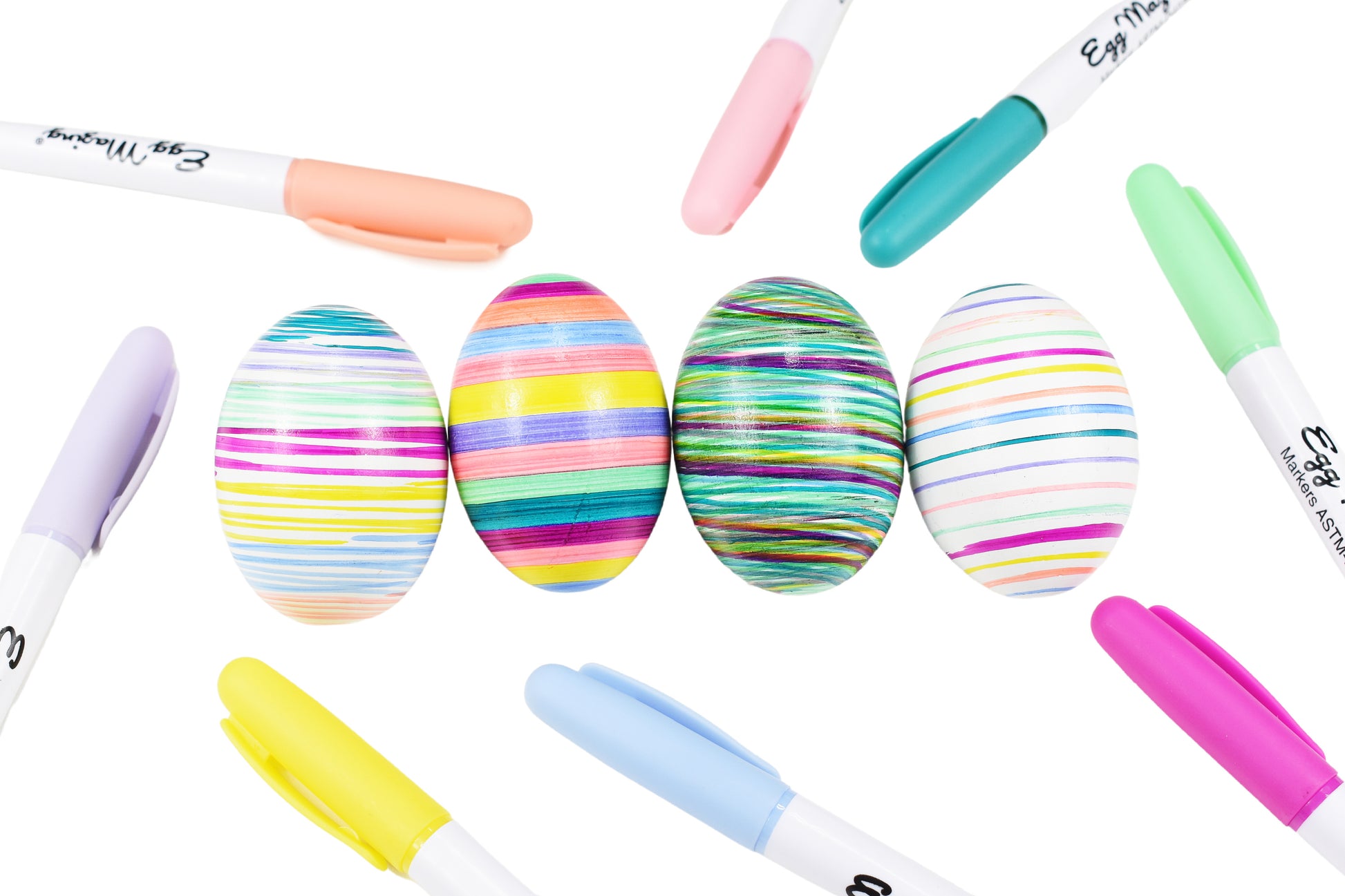 Image showing a variety of colorful markers and four striped eggs. Colors include bright pink, mint green, light blue, peach, turquoise, yellow, light pink, and light purple. 