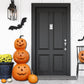 Image showing a porch scene with a black front door, yellow flowers in a pot, three small pumpkins, and a stack of three pumpkins next to the door. 
